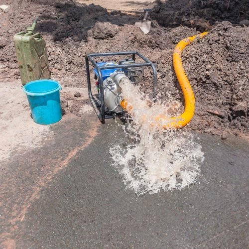 Water pump ejecting water into muddy construction site.