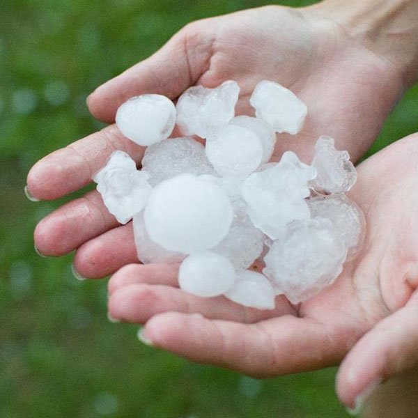 Hands holding large hailstones outdoors.