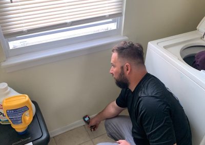 Man inspecting laundry room with digital meter.